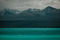 Дивовижний новозеландський краєвид з бірюзовою морською водою і скелястими горами з снігом на верхівках до хмарного неба. — стокове фото
