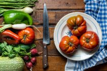 Frisches Bio-Gemüse auf einem dunklen Holztisch mit Tomaten in einer Schüssel und einem Messer — Stockfoto
