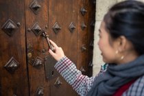 Side view of black-haired female tourist in casual clothing exploring creative oblong metal handle of old door — Photo de stock