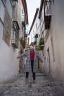 From below of overjoyed female traveler in casual clothing smiling and standing while raising hands and looking in camera among lane at Albaicin in Granada — Stock Photo