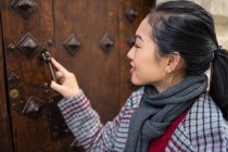 Curious female traveler in casual wear clattering in ancient door at city street — Stock Photo