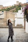 Asian female traveler in warm wear smiling among old buildings near big castle — Stock Photo