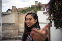 Азиатская женщина в теплой одежде улыбается среди старых зданий возле большого замка — стоковое фото