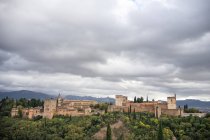 Poderoso castelo antigo rocked Alcazaba de Alhambra em grande supercrescido de árvores verdes perto da cidade velha com montanhas e céu nublado em Granada — Fotografia de Stock