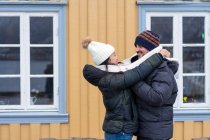 Multiethnic happy couple of tourists in warm clothing embracing near rural house — Stock Photo