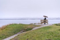 Mujer sentada bajo paraguas en la costa - foto de stock