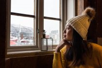 Pensive Asian female tourist in warm clothing admiring in view through window — Stock Photo