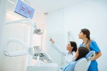 Стоматолог и ассистент, показывающий клиенту на стуле структуру зубов на картинке — стоковое фото