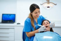 Dentista y asistente examinando la boca del paciente en silla con t - foto de stock