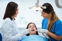 Dentista e assistente examinando boca de paciente em cadeira com t — Fotografia de Stock
