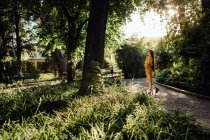 Азиатская женщина с длинными темными волосами идет вдоль освещенной солнцем дороги и травяного луга глядя на камеру через плечо — стоковое фото
