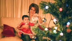 Madre jugando con el bebé cerca del árbol de Navidad - foto de stock