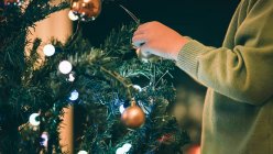 Imagen recortada de Niño decorando árbol de Navidad en la noche - foto de stock