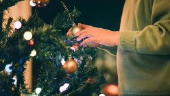 Zugeschnittenes Bild eines Jungen, der abends den Weihnachtsbaum schmückt — Stockfoto