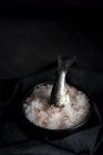 Вкусный хвост скумбрии, торчащий из тарелки с солью на черном фоне — стоковое фото