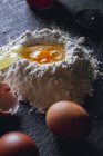 Nahaufnahme von zerbrochenem Ei in Mehl auf strukturierter schwarzer Oberfläche — Stockfoto