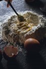 Mão de pessoa com garfo misturando ovo e farinha enquanto prepara massa para massas na mesa preta — Fotografia de Stock