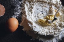 Close-up of mixing egg and flour while preparing dough for pasta on black table — Stock Photo