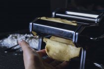 Крупный план человека ручной прокатки теста через макароны машины при подготовке свежей домашней пасты на столе — стоковое фото