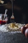 Fork mixing egg and flour while preparing dough for pasta on black table — Stock Photo