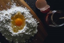 Top view of broken egg in flour on textured black surface with glass pot — Stock Photo