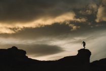 From below of male silhouette in motion on mountain with beautiful cloudy sky on background — Stock Photo