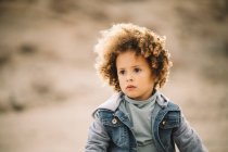 Adorable casual curly ethnic child thoughtfully looking away on blurred background — Stock Photo