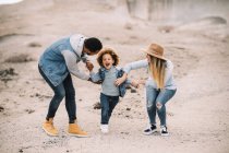 Happy multiracial parents playing with smiling adorable curly ethnic toddler at sandy desert — Stock Photo