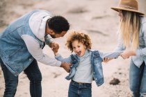 Happy multiracial parents playing with smiling adorable curly ethnic toddler at sandy desert — Stock Photo