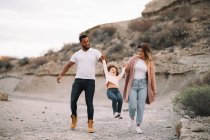 Felice madre e padre diversificato con bambino riccio passeggiando sulla natura durante il giorno — Foto stock