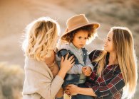 Cheerful women with cute casual toddler with curly hair resting in nature at daytime — Stock Photo
