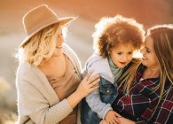 Cheerful women with cute casual toddler with curly hair resting in nature at daytime — Stock Photo