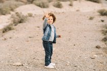 Adorable curly ethnic child dressed in casual clothes waving hand on blurred background — Stock Photo