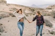 Frau mit Hut hält zärtlich Händchen mit Freundin im karierten Hemd und lächelt, als ginge sie in der Natur — Stockfoto