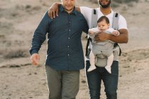 Обрізані випадкові чоловіки тримають маленьку спокійну дитину в носії під час прогулянки на природі вдень — стокове фото
