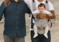 Zugeschnitten von lässigen Männern, die ein kleines ruhiges Baby im Tragetuch tragen, während sie tagsüber in der Natur spazieren — Stockfoto