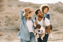 Felice casuale moglie caucasica e nero sorridente marito portando i bambini sulla natura durante il giorno — Foto stock