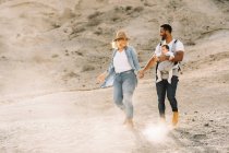 Homme joyeux portant petit bébé et tenant la main avec femme blonde tout en marchant dans le désert sablonneux — Photo de stock