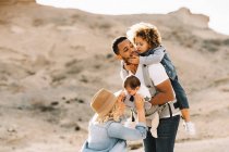 Glücklich lässig kaukasische Frau und schwarz lächelnder Ehemann spielen tagsüber mit niedlichen Kindern in der Natur — Stockfoto