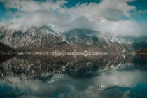 Безмятежный пейзаж неподвижного озера, отражающего яркое облачное небо, окруженное снежными горами в Халлштатте — стоковое фото