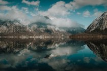 Serena paisagem deslumbrante de lago imóvel refletindo céu nublado brilhante cercado por montanhas nevadas em Hallstatt — Fotografia de Stock