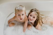 Niños divertidos jugando con espuma en el baño - foto de stock