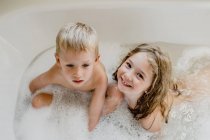 Crianças engraçadas brincando com espuma no banho — Fotografia de Stock