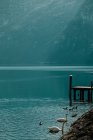 Paisaje sereno en el muelle de madera vacío en aguas cristalinas que reflejan el cielo y las montañas nevadas en el día brillante en Hallstatt - foto de stock