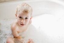 Miúdo bonito brincando com espuma no banho — Fotografia de Stock