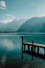 Paesaggio sereno sul molo di legno vuoto in acque cristalline calme che riflettono cielo e montagne innevate durante il giorno luminoso a Hallstatt — Foto stock