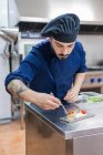 Concentrated professional male chef garnishing and finishing delicious dish ready for serving while working at metal counter in restaurant kitchen — Stock Photo
