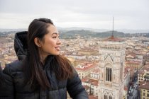 Happy Asian woman smiling and looking away while standing on Brunelleschi Dome against old Florence streets during trip in Italy — Stock Photo
