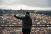 Rückansicht einer Frau, die ihr Smartphone benutzt, um ein Selfie zu machen, während sie auf der Aussichtsplattform der Kathedrale Santa Maria del Fiore in den alten Straßen von Florenz steht, Italien — Stockfoto