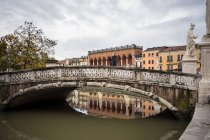Turista en ropa de abrigo en el puente antiguo balanceado sobre el estanque con edificios antiguos y estatuas en el fondo en el parque Prato della Valle en Padova en Italia - foto de stock